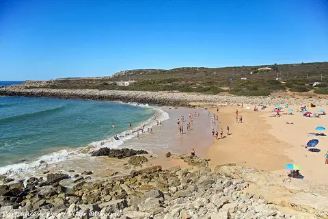 Praia da Ingrina com areal, rochas em primeiro plano e mar calmo sob céu azul
