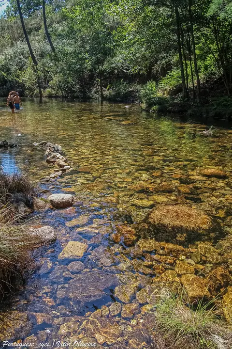 Praia fluvial de Poço de Mato com água transparente sobre rochas e vegetação nas margens