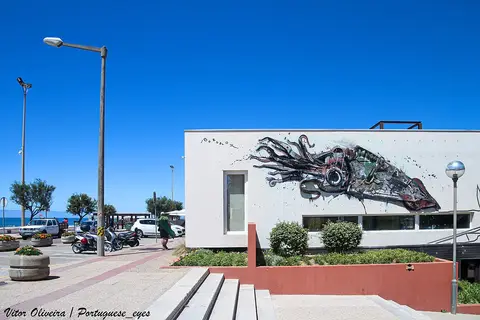 Edifício branco com mural de peixe junto ao parque de estacionamento da Praia da Tocha, com o mar ao fundo