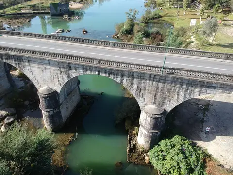 Vista aérea da Ponte do Bico, com arcos de pedra sobre rio de águas verdes e margens arborizadas.