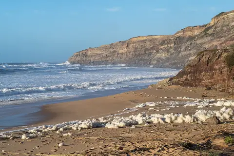 Praia de Valmitão com falésias, ondas e espuma do mar sobre a areia