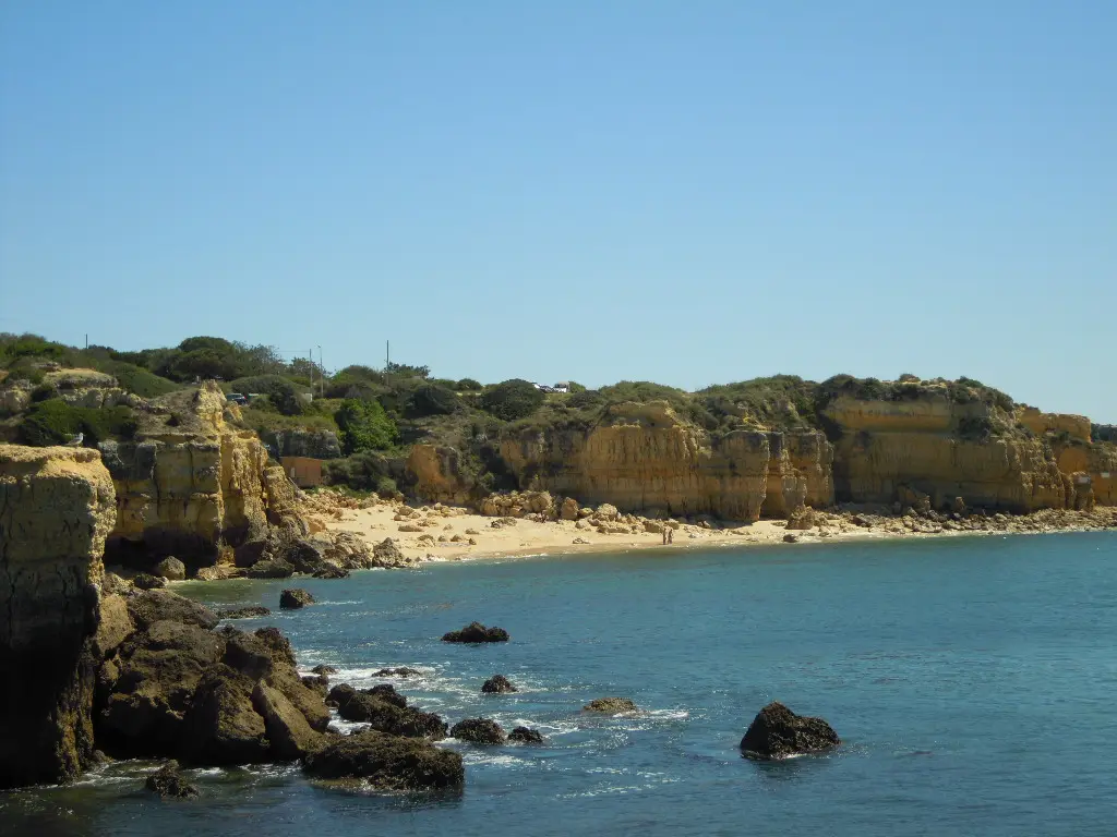 Praia do Castelo em Albufeira, com falésias douradas, rochas no mar e areia ao fundo