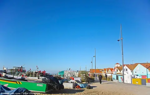 Praia de Angeiras com barcos de pesca, armadilhas e casas coloridas junto ao areal sob céu azul