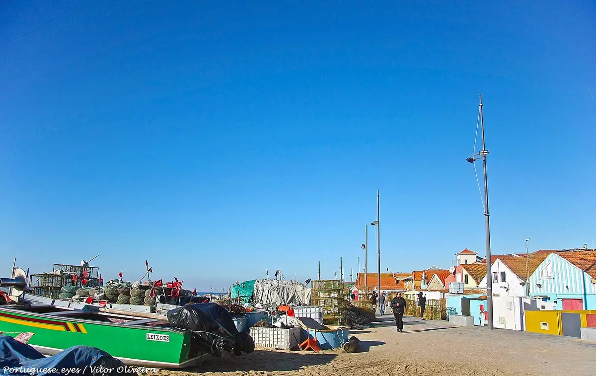 Praia de Angeiras com barcos de pesca, armadilhas e casas coloridas junto ao areal sob céu azul