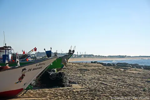 Barco de pesca com redes na areia da praia de Angeiras, com o mar e rochas ao fundo