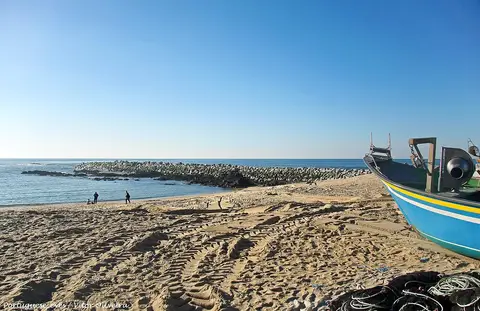 Praia de areia em Angeiras com barco de pesca colorido e quebra-mar de rochas ao fundo