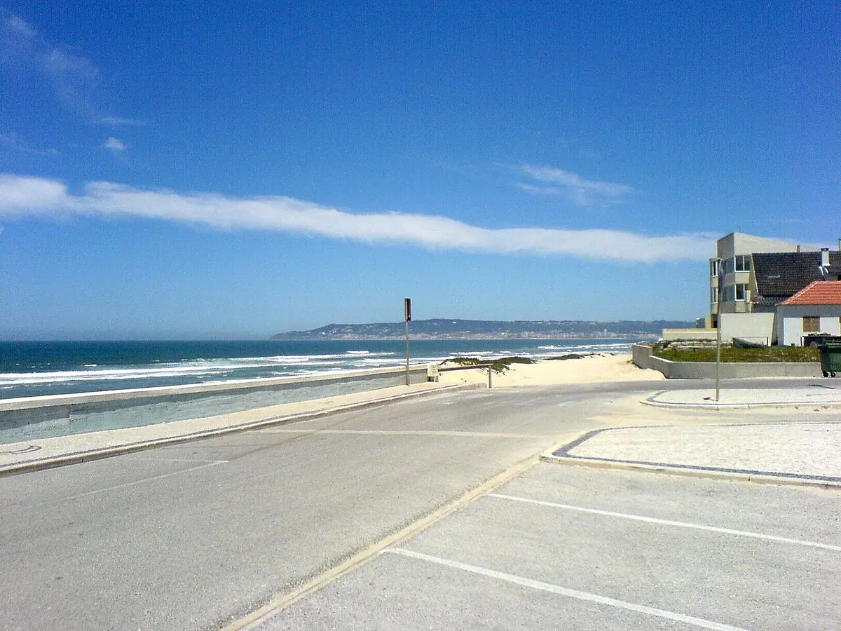 Estrada junto à praia da Costa de Lavos, com mar, areal e edifícios ao fundo sob céu azul