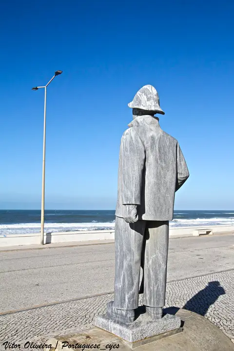 Estátua de pescador de costas junto à marginal, com o mar da Costa de Lavos ao fundo