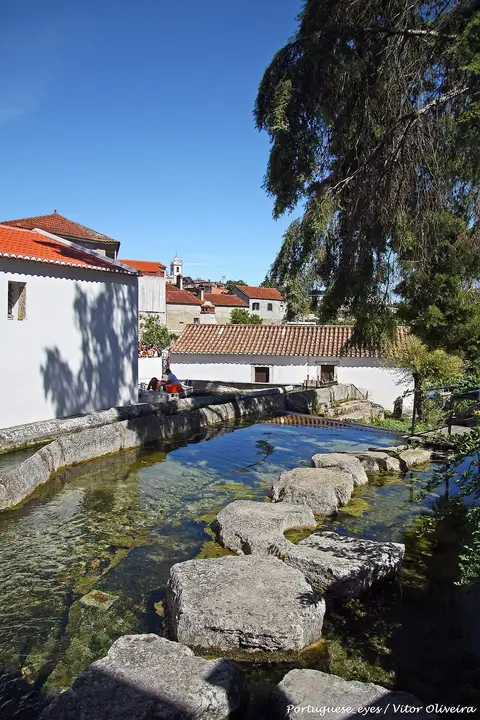 Tanque de água cristalina com pedras de passagem junto a casas brancas de telhado vermelho em Ançã