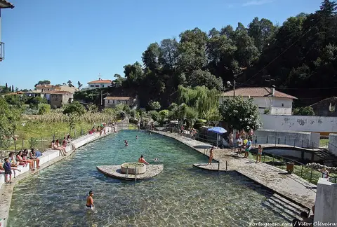 Praia fluvial de Ançã com piscina natural de água pouco profunda rodeada de vegetação e casas.