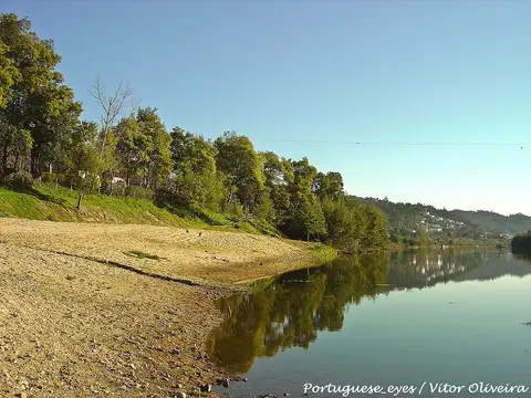 Praia fluvial do Reconquinho, com areal junto ao rio calmo e árvores na margem