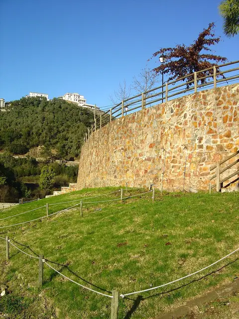 Muro de pedra com guarda de madeira e relvado junto à praia fluvial do Reconquinho