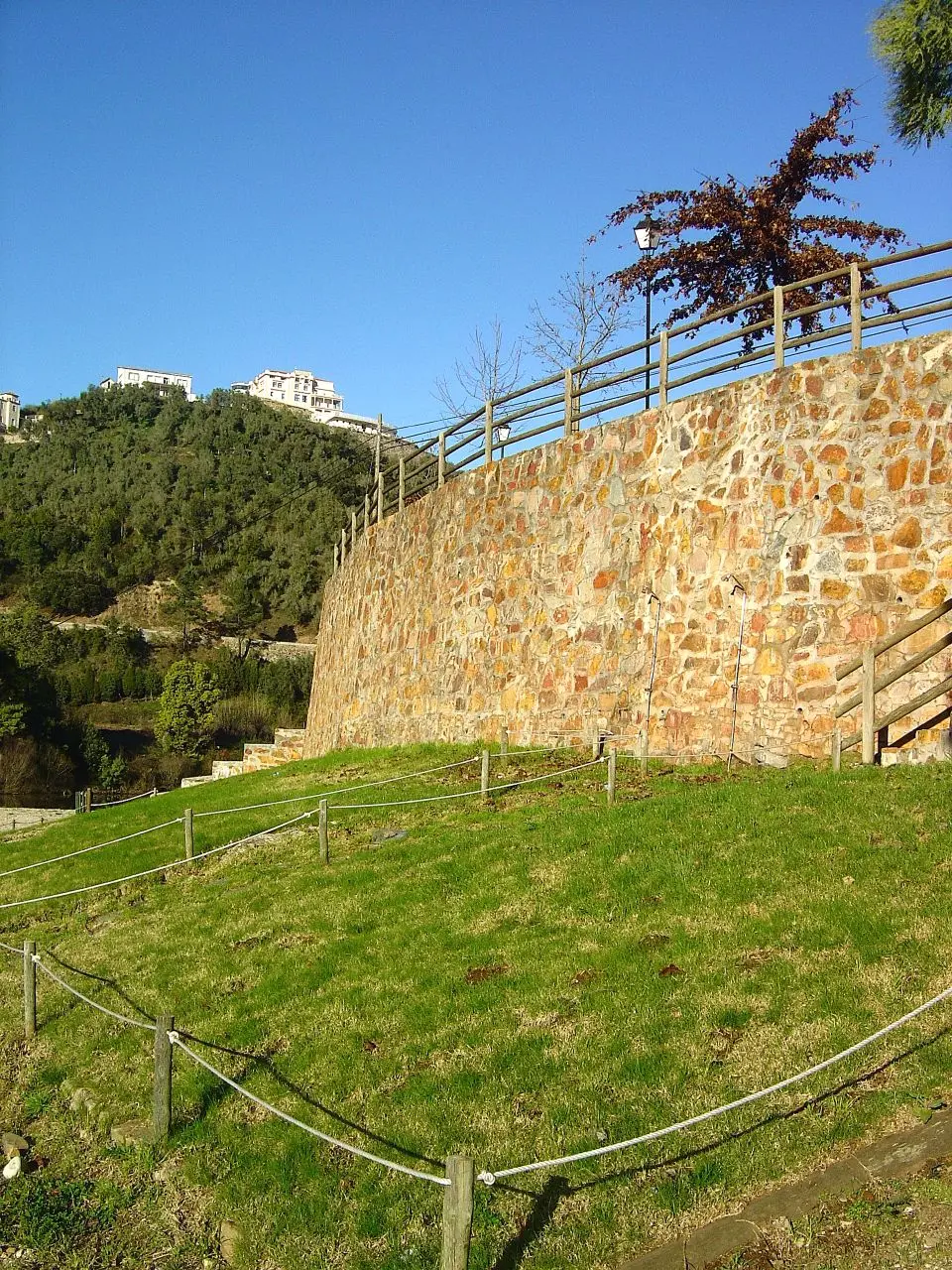 Muro de pedra com guarda de madeira e relvado junto à praia fluvial do Reconquinho
