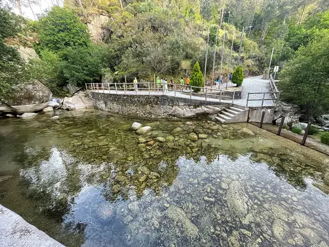 Praia fluvial de Lapa dos Dinheiros com água transparente sobre pedras e passadiço em pedra