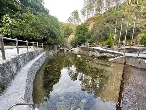 Praia fluvial de Lapa dos Dinheiros, com açude de água transparente, muros de pedra e vegetação em volta