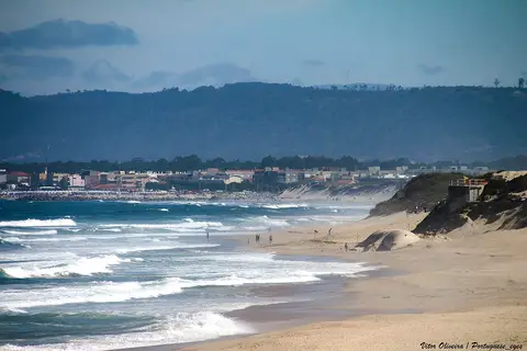 Praia da Estela com areal extenso, ondas e dunas, e povoação ao fundo junto à costa