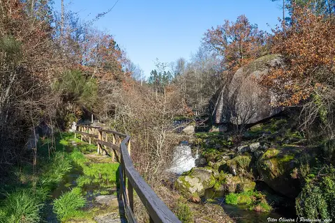 Passadiço de madeira junto a ribeiro com rochas e vegetação na zona de lazer da Ucha