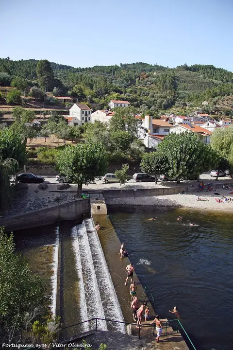 Praia fluvial de São Sebastião da Feira com açude, banhistas ao longe e aldeia na encosta