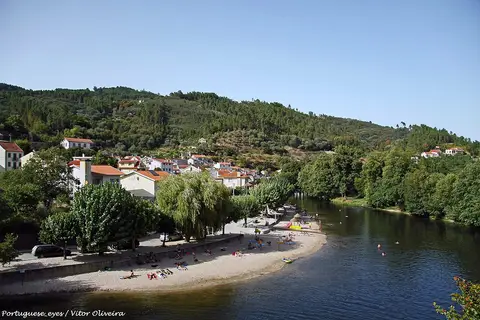 Praia fluvial de São Sebastião da Feira, com areal junto ao rio e aldeia na encosta arborizada