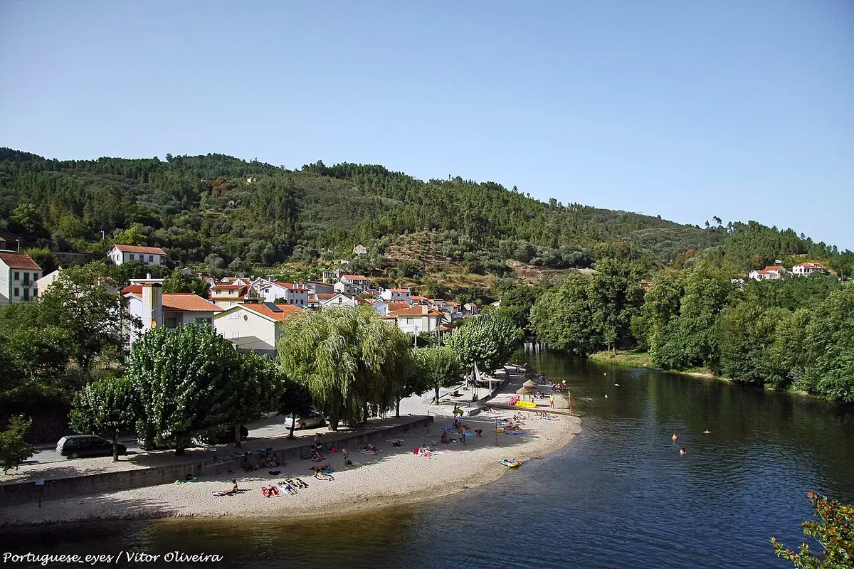 Praia fluvial de São Sebastião da Feira, com areal junto ao rio e aldeia na encosta arborizada