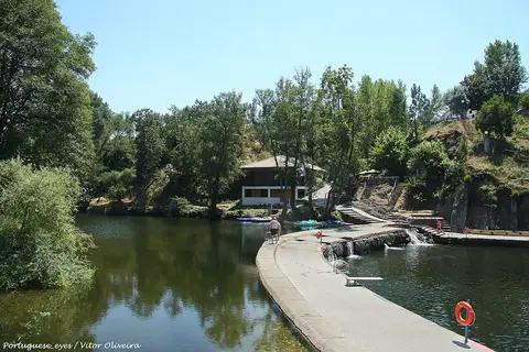 Praia fluvial de Côja com açude, passadiço sobre o rio e edifício de apoio rodeado de árvores