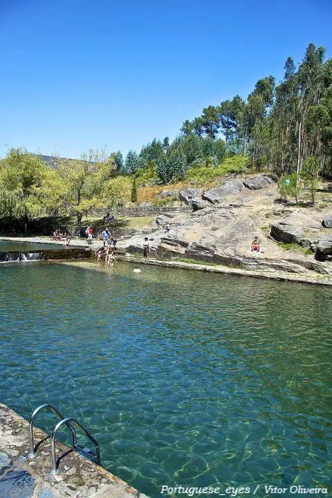 Praia fluvial do Poço da Corga, com água esverdeada, rochas e escada de acesso