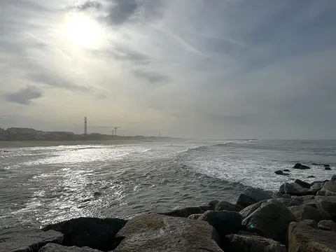 Praia da Baía em Espinho com esporão de rochas, ondas e sol entre nuvens