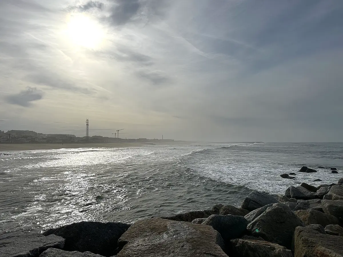 Praia da Baía em Espinho com esporão de rochas, ondas e sol entre nuvens