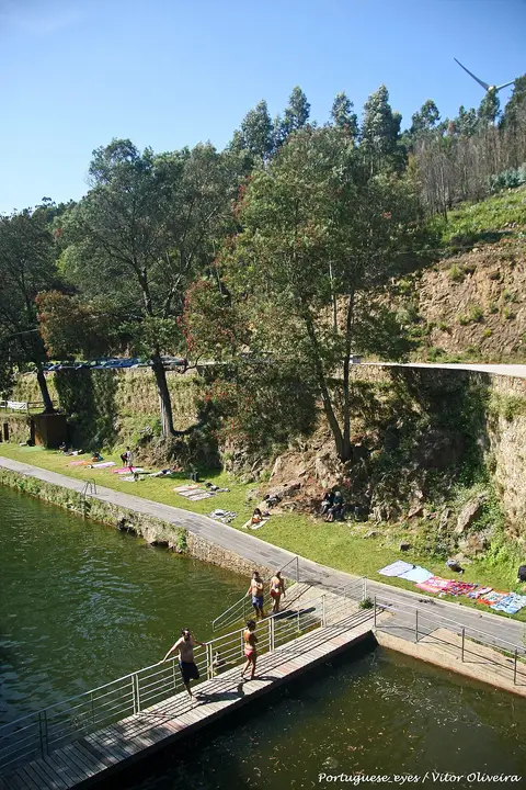 Praia fluvial de Louçainha com plataforma de madeira sobre a água, relva e encosta arborizada
