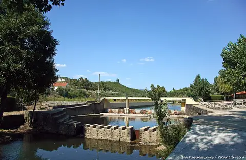 Praia fluvial da Aldeia Ruiva com açude, escadas de acesso à água e ponte ao fundo