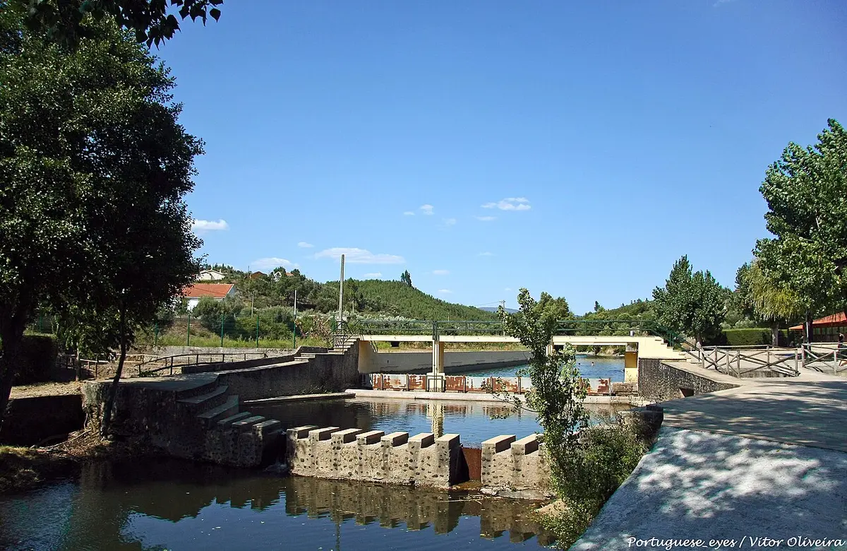 Praia fluvial da Aldeia Ruiva com açude, escadas de acesso à água e ponte ao fundo