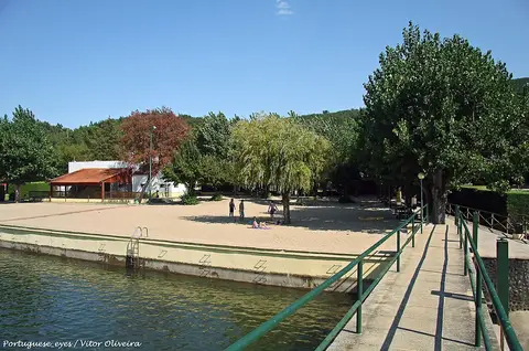 Praia fluvial da Aldeia Ruiva com areal, passadiço metálico sobre a água e árvores em redor
