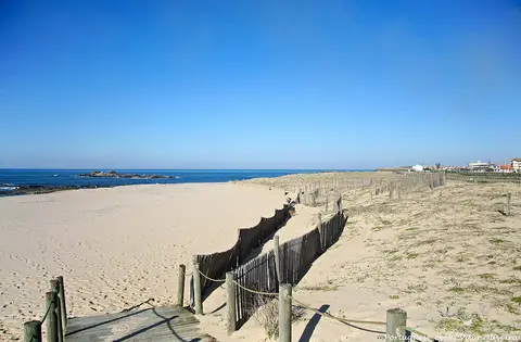 Praia da Memória com areal amplo, paliçadas de madeira nas dunas e mar calmo sob céu azul