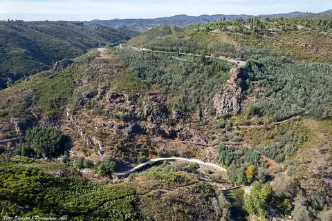Vista aérea do vale do Penedo Furado, com encostas verdes, trilhos e o rio ao fundo