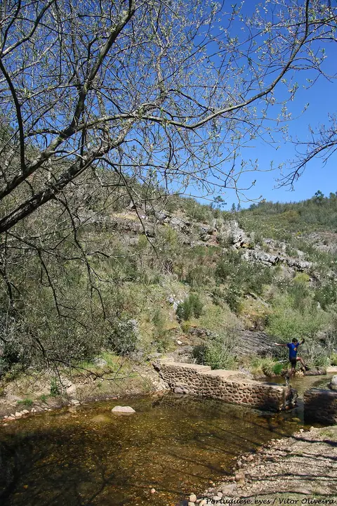 Praia fluvial do Penedo Furado com açude de pedra, água limpa e encosta de vegetação