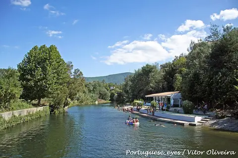 Praia fluvial da Senhora da Graça em Serpins, com rio, plataforma de madeira e vegetação envolvente.