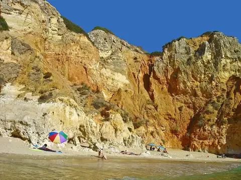 Praia do Camilo com falésias douradas, areia e chapéus de sol coloridos junto ao mar