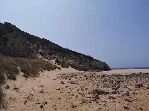 Praia das Furnas com areal, pedras e arriba rochosa coberta de vegetação junto ao mar