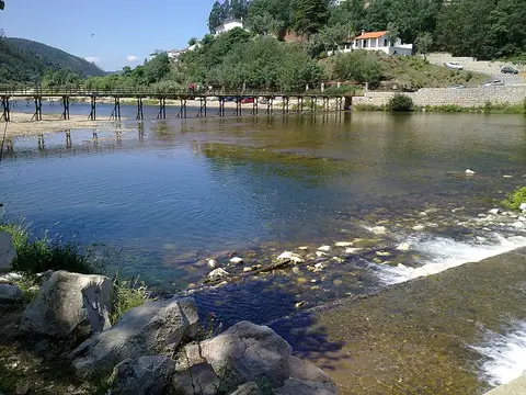 Praia fluvial de Palheiros e Zorro com ponte de madeira sobre o rio e encostas verdes
