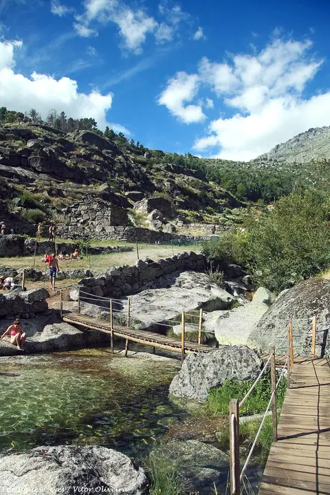 Praia fluvial de Loriga com passadiço de madeira sobre água transparente entre rochas de granito