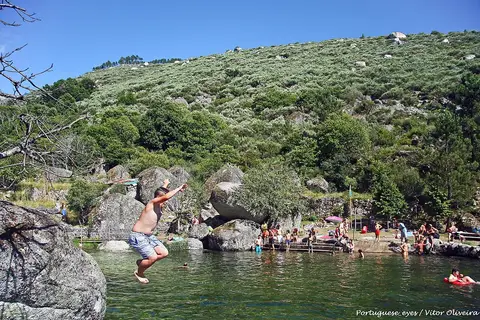 Praia fluvial de Loriga, com rapaz a saltar de uma rocha para a água e encosta verde ao fundo