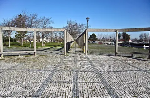 Passeio em calçada portuguesa com pérgola de betão no Cais do Bico, Murtosa, sob céu azul.