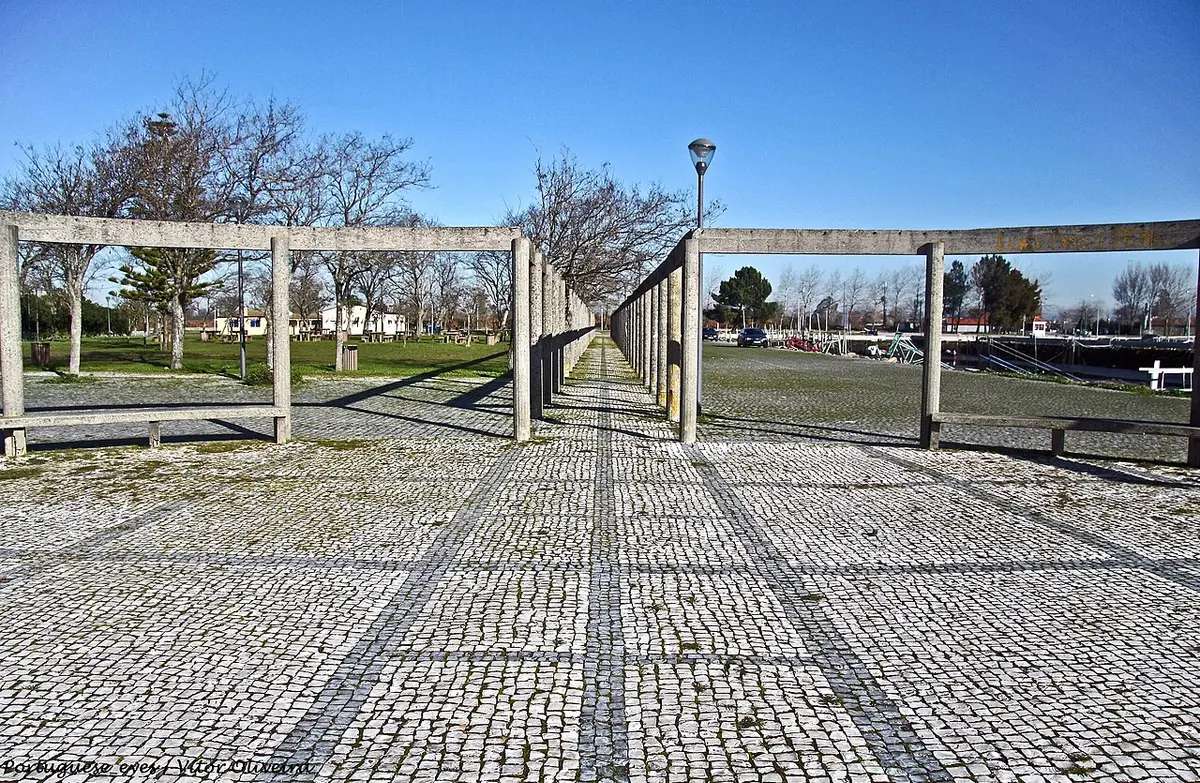 Passeio em calçada portuguesa com pérgola de betão no Cais do Bico, Murtosa, sob céu azul.