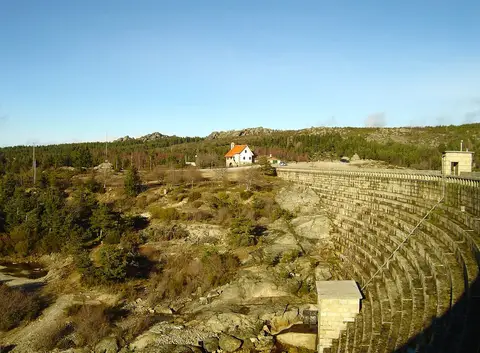 Barragem do Vale do Rossim em pedra, com casa de telhado vermelho e paisagem rochosa da serra.