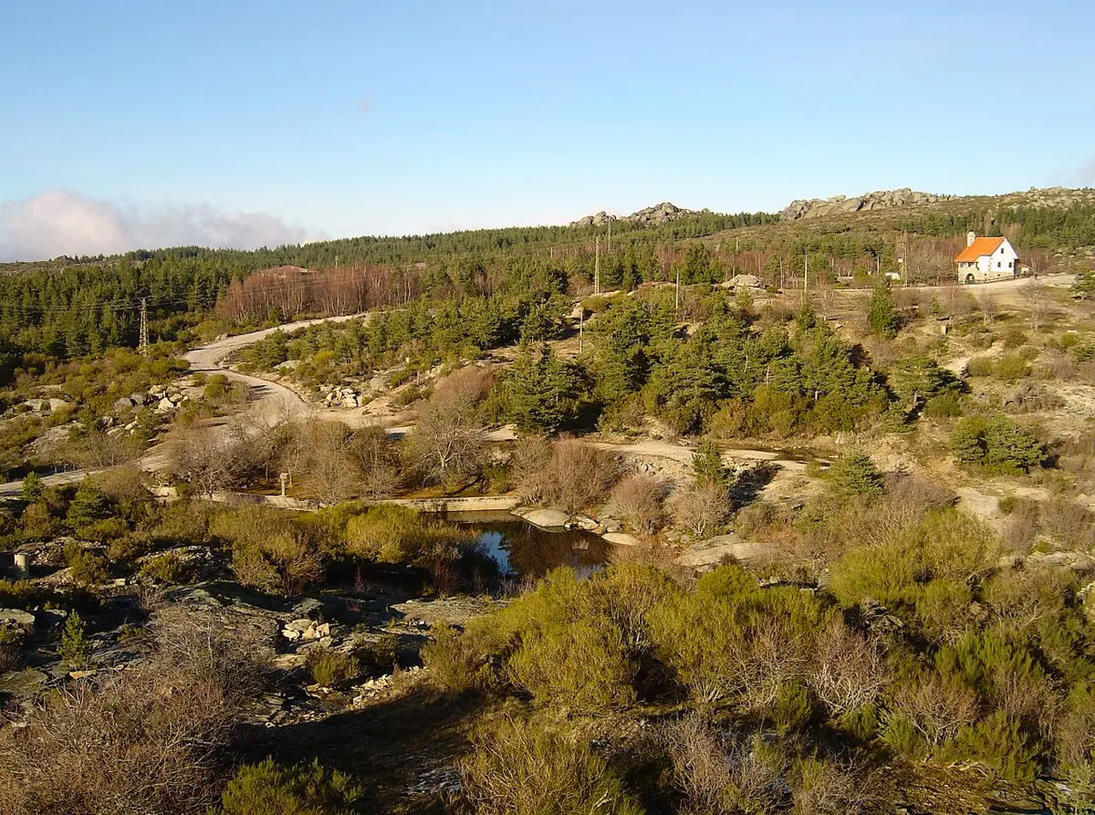 Paisagem serrana do Vale do Rossim com pinhal, rochedos, pequeno curso de água e casa branca ao fundo