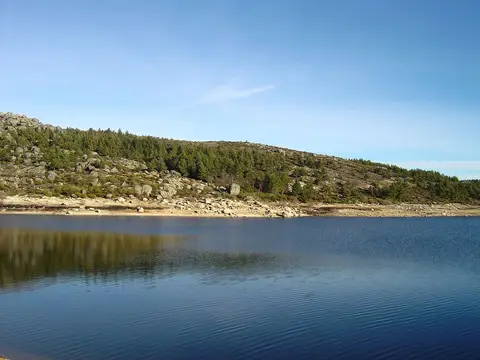 Albufeira do Vale do Rossim com águas calmas, margens rochosas e encosta com pinheiros sob céu azul