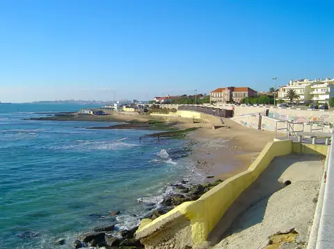 Praia da Parede com areal, rochas e passeio marítimo junto ao mar azul, em dia de céu limpo