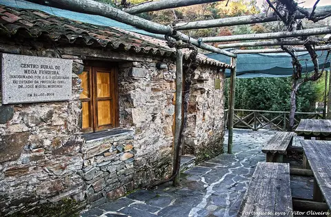 Centro Rural de Mega Fundeira: casa de xisto com placa, latada e mesas de madeira no exterior