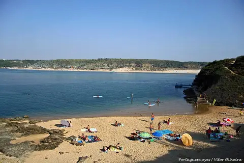 Praia da Franquia em Vila Nova de Milfontes, com areal, banhistas ao longe e águas calmas do estuário.