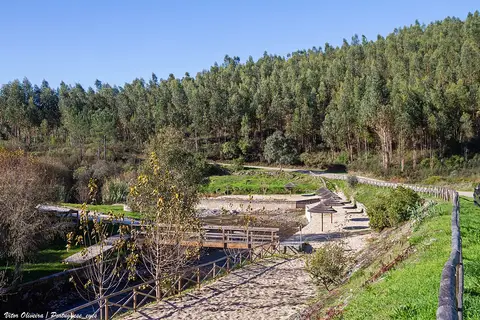 Praia fluvial do Boiçô com passadiços de madeira, caminho de areia e encosta de eucaliptos ao fundo